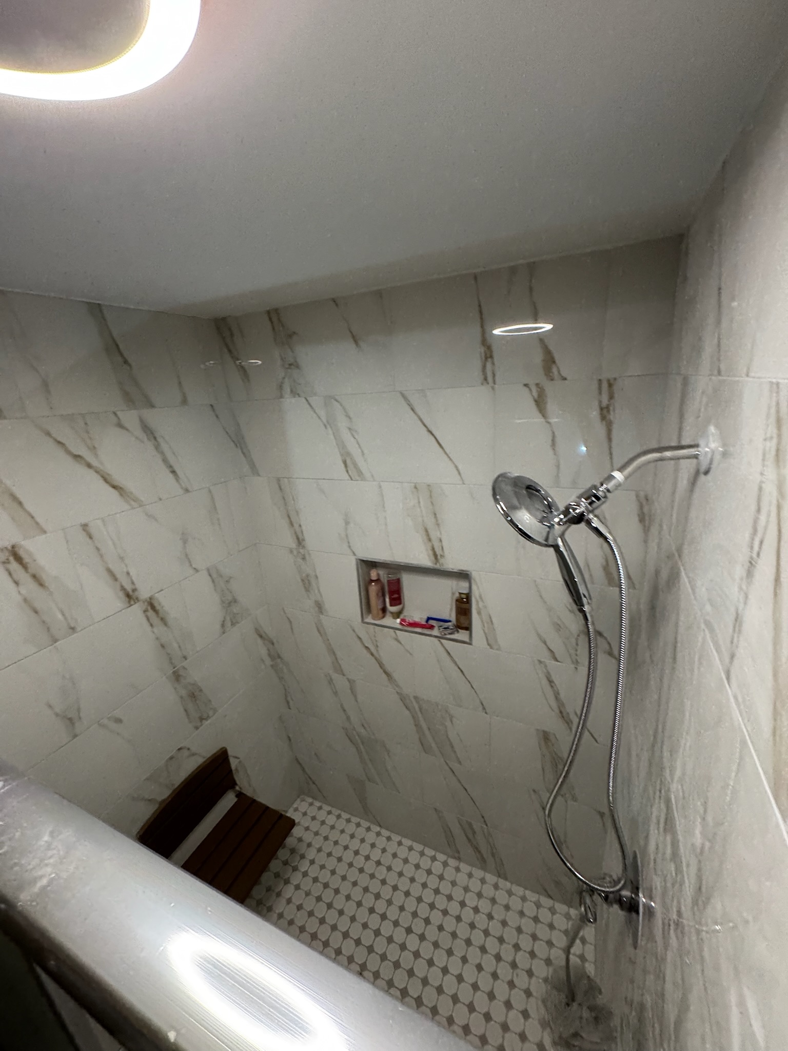 Clean marble-tiled shower with handheld sprayer and built-in bench after professional restoration
